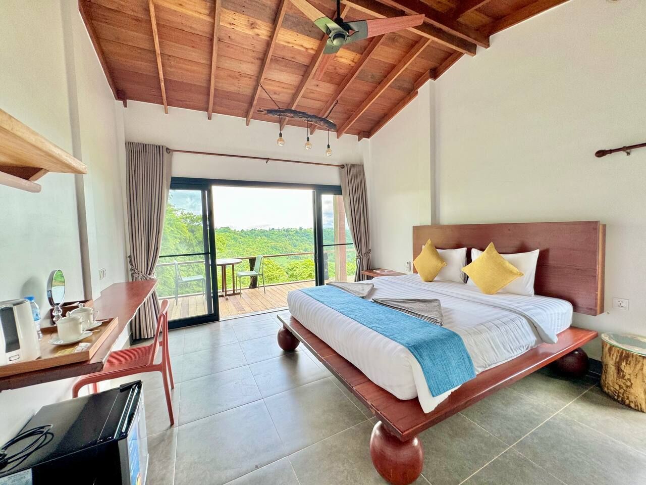 A bedroom with a large bed, a desk, and a balcony with a view.