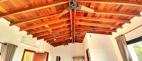 Una stanza con soffitto in legno, una ventola a soffitto, una scrivania con una sedia e una finestra con tende.