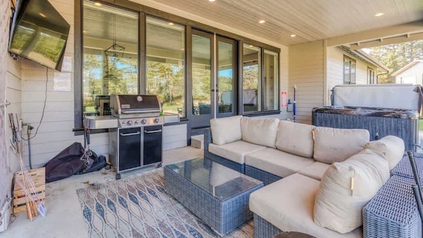 A covered outdoor living area with a grill, sofa, and glass coffee table.