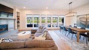 A modern living room with a large sectional sofa, a dining table with chairs, and a fireplace.