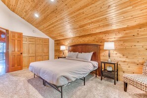 Un dormitorio con techo de madera, una cama, dos mesitas de noche con lámparas, una silla y una puerta a un balcón.