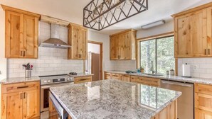A kitchen with wooden cabinets, a granite countertop, a stainless steel range hood, and a window providing natural light.