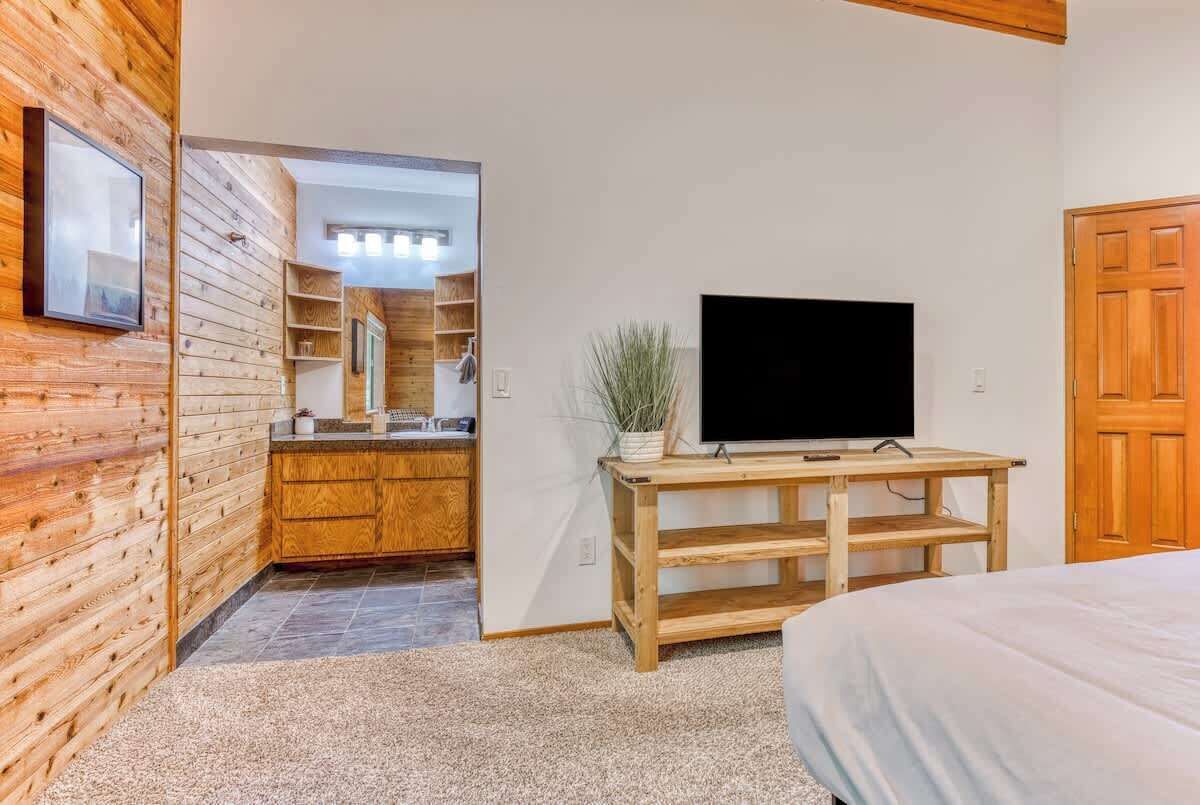 A bedroom with a bed, a TV on a wooden stand, a wooden wardrobe, and a mirror.