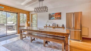 A spacious kitchen with a large wooden table, a stainless steel refrigerator, and a hanging light fixture.