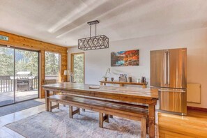 A spacious kitchen with a large wooden table, a stainless steel refrigerator, and a hanging light fixture. - Great Blue Lodge - Scenic escape | Hot tub & sauna (Government Camp)