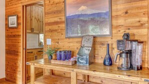 A wooden interior with a kitchen counter, a framed picture of a mountain, and a coffee maker.