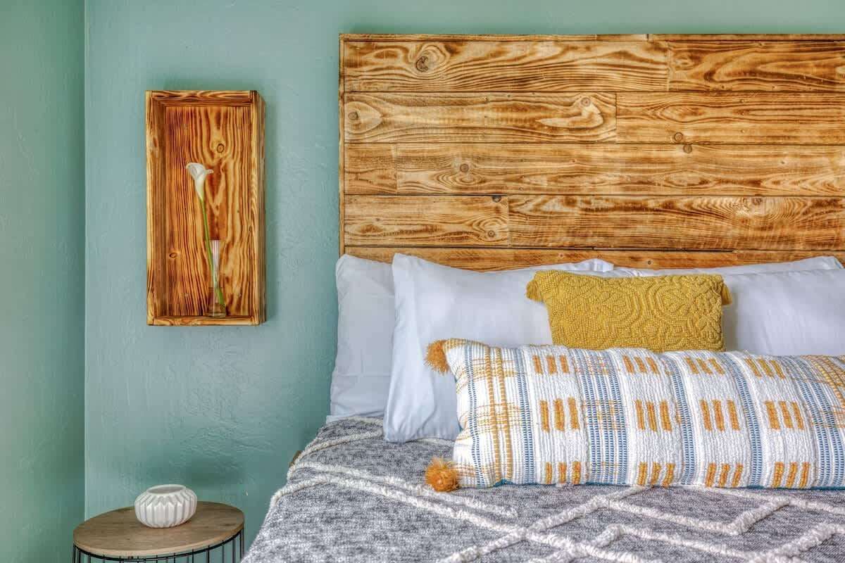 A bedroom with a wooden headboard, a patterned throw pillow, a white pillow, and a gray blanket.