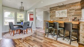 Un comedor con una mesa redonda y sillas, una zona de bar con taburetes, y una pared de piedra decorativa con un mapa mundial.