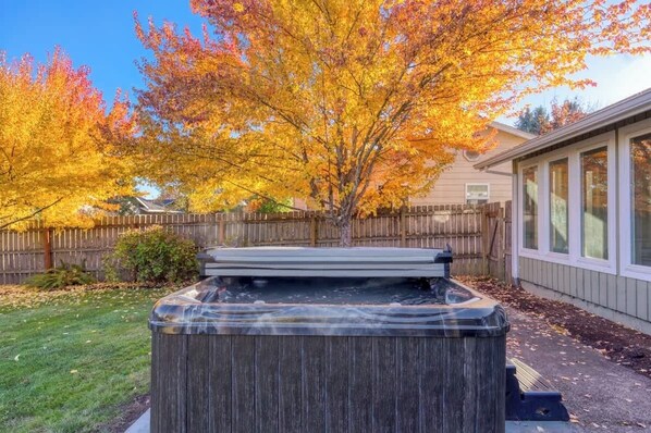 A hot tub in a backyard with a wooden fence and trees with autumn foliage.