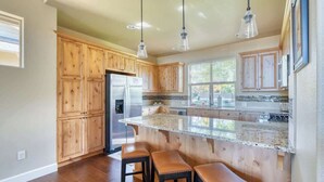 Una cocina con armarios de madera, un refrigerador de acero inoxidable, una encimera de granito e iluminación colgante.