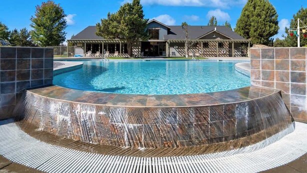 Una piscina con cascada, rodeada por un porche cubierto con sillones de descanso.