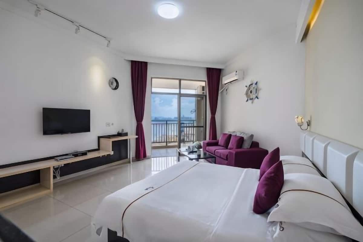 Una habitación de hotel con cama, televisión, sofá, mesa de centro y balcón con cortinas.