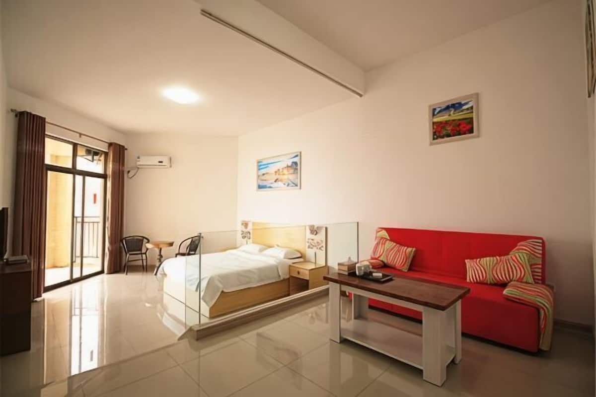 Una habitación de hotel con una cama, un sofá rojo, una mesa de centro, un televisor y un cuadro en la pared.