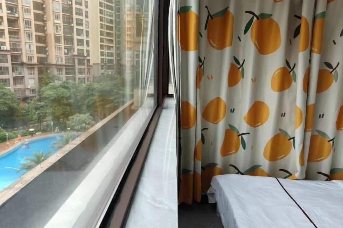 Habitación de hotel con un ventanal grande, una cama y cortinas con estampado de frutas.