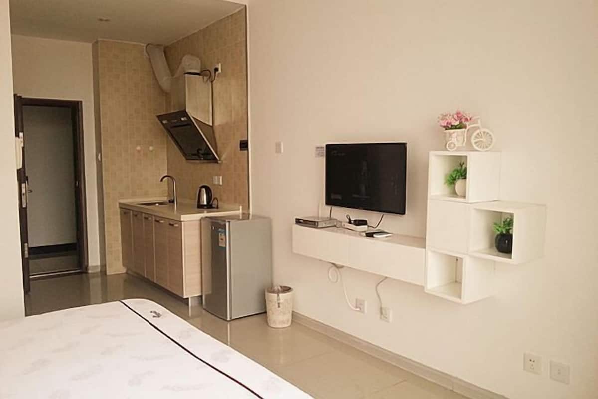 Una cocina moderna con refrigerador, microondas y estufa, un televisor montado en la pared y un pequeño estante con objetos decorativos.