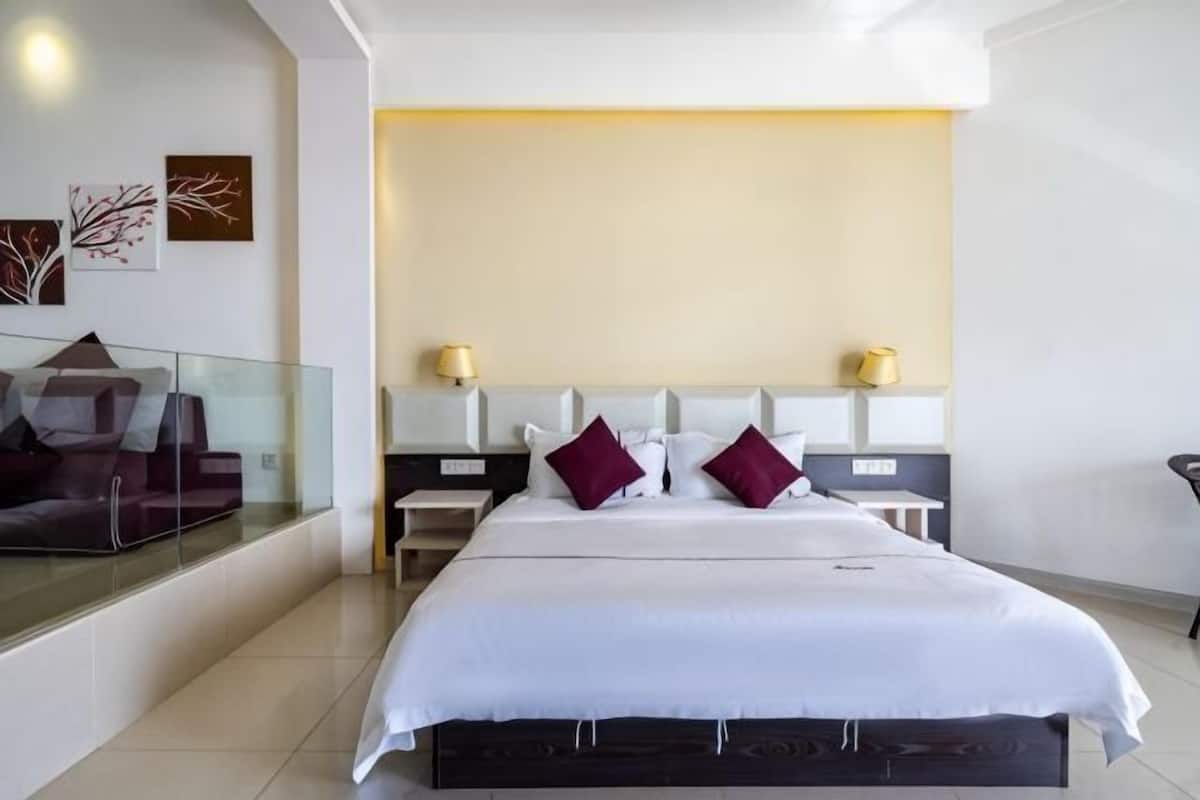 Una habitación de hotel moderna con una cama grande, un separador de vidrio, una mesita de noche y una lámpara de pared.