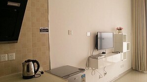 Habitación de hotel con televisor de pantalla plana, una mesita con tetera, estación de carga y espejo en la pared.