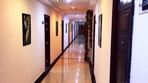 Un largo pasillo pulido con puertas a ambos lados, enmarcado por paredes de colores claros y un suelo reflectante.