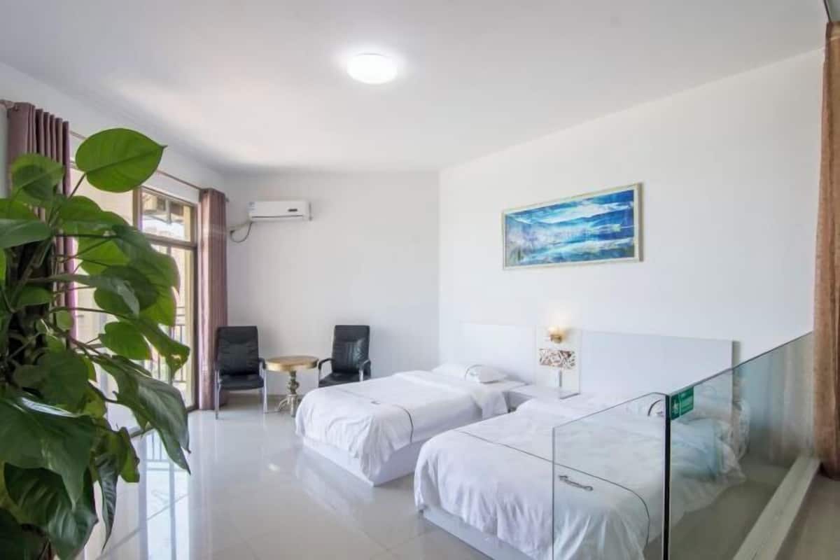Habitación de hotel con dos camas, un escritorio, una silla, un ventanal con cortinas, un cuadro en la pared y una planta en maceta.