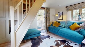 A room with a staircase, a teal sofa with yellow cushions, a cowhide rug, and a window with curtains.
