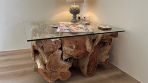 A glass-top table with a wooden base, a lamp, and some magazines on it.
