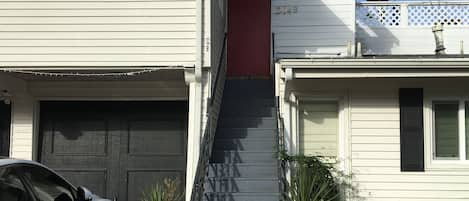 A two-story house with a garage, a staircase leading to the second floor, and a balcony with a lattice railing.