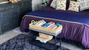 Ein Schlafzimmer mit einem Bett, einem Schminktisch, einem Nachttisch, einer Lampe und einer Wand mit einem Buddha-Gemälde.