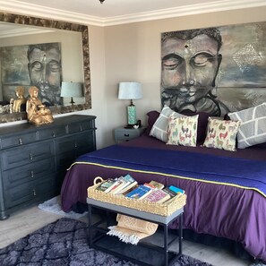Une chambre à coucher comprenant un lit, une commode, une table de chevet, une lampe et un mur orné d’un tableau représentant un Bouddha.