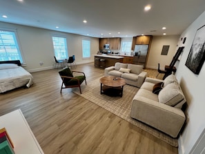 Amplia sala de estar con un sofá, sillones y una mesa de centro. Se observa una cocina con electrodomésticos modernos al fondo.