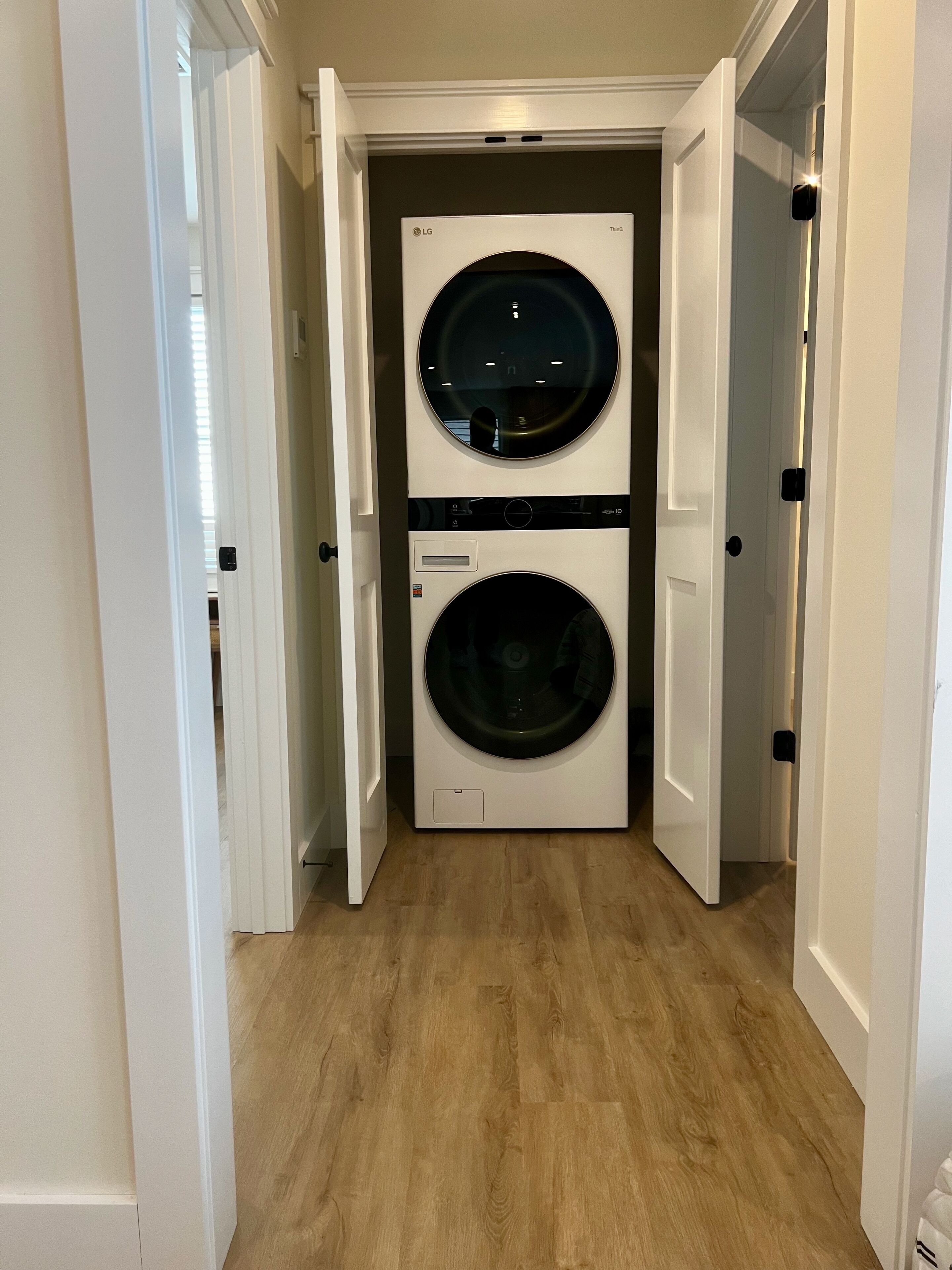 A laundry room with two front-loading washing machines and dryers, wooden flooring, and white walls.