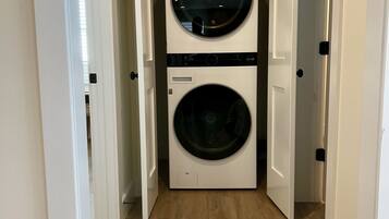 A laundry room with two front-loading washing machines and dryers, wooden flooring, and white walls.