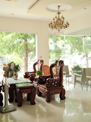 Una habitación con muebles de madera ornamentados, un candelabro y ventanas grandes con vistas a zonas verdes.