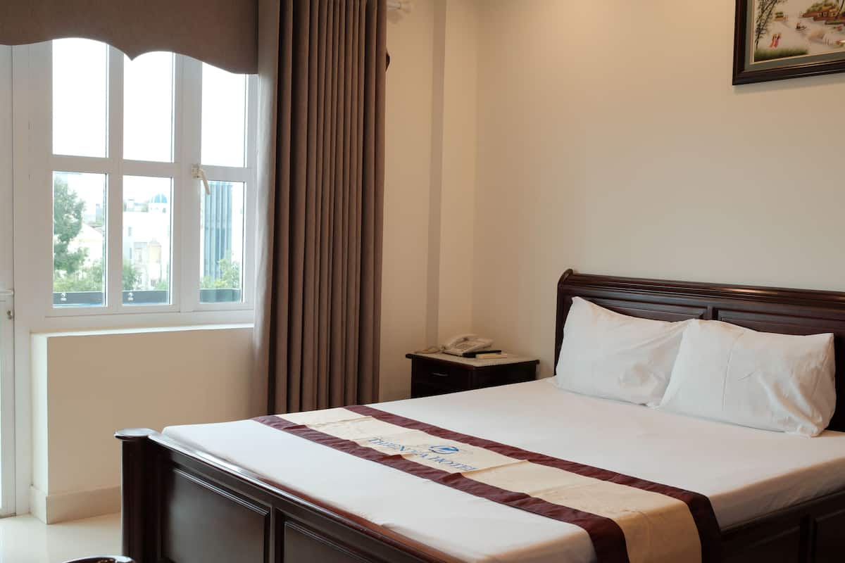 Hotellihuone, jossa on suuri sänky, yöpöytä, puhelin ja ikkuna, jossa on verhot.