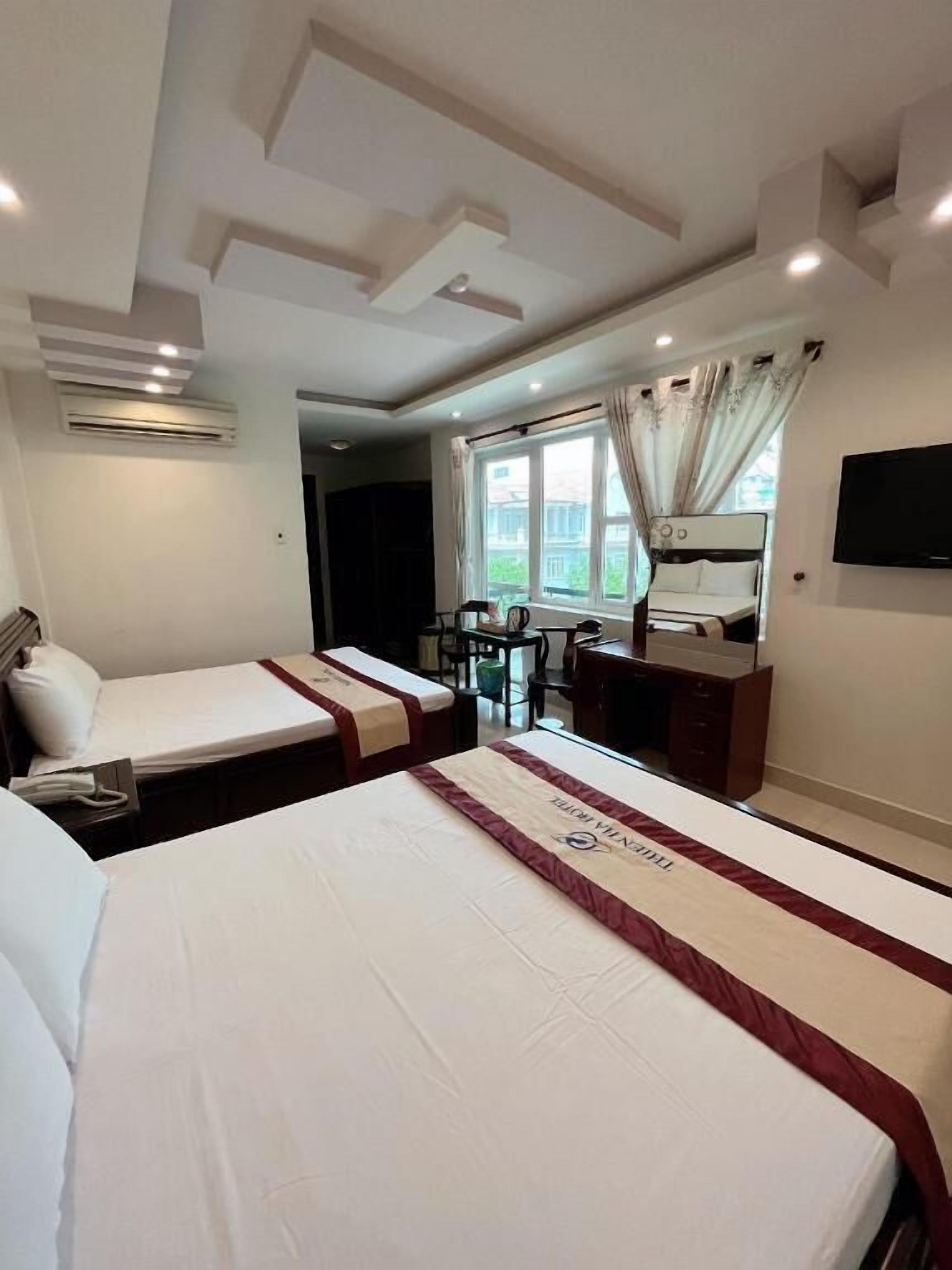Habitación de hotel con dos camas, un escritorio, una silla, un televisor y una ventana con cortinas.