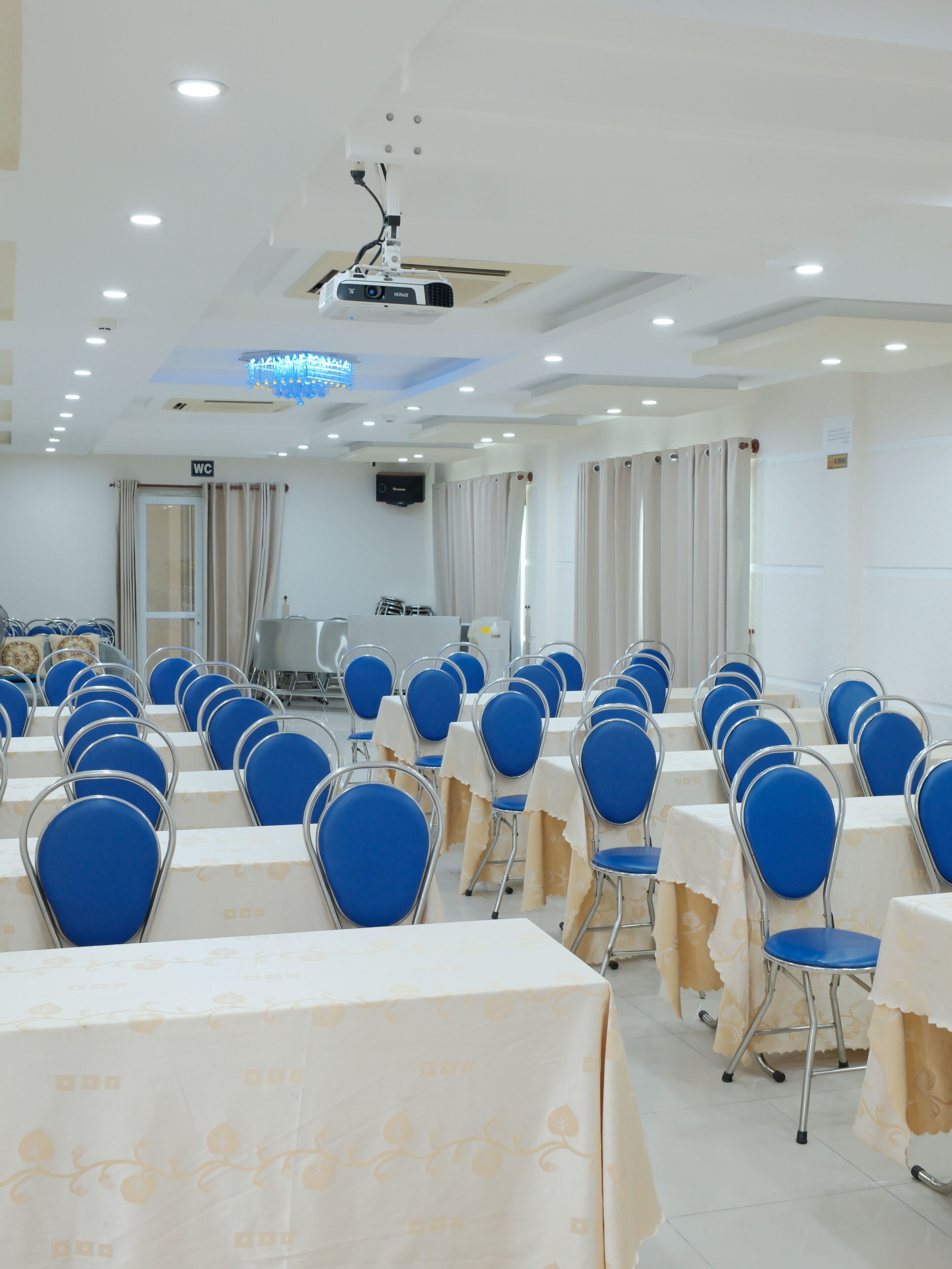 A conference room with rows of tables and chairs, a projector, and a TV screen.
