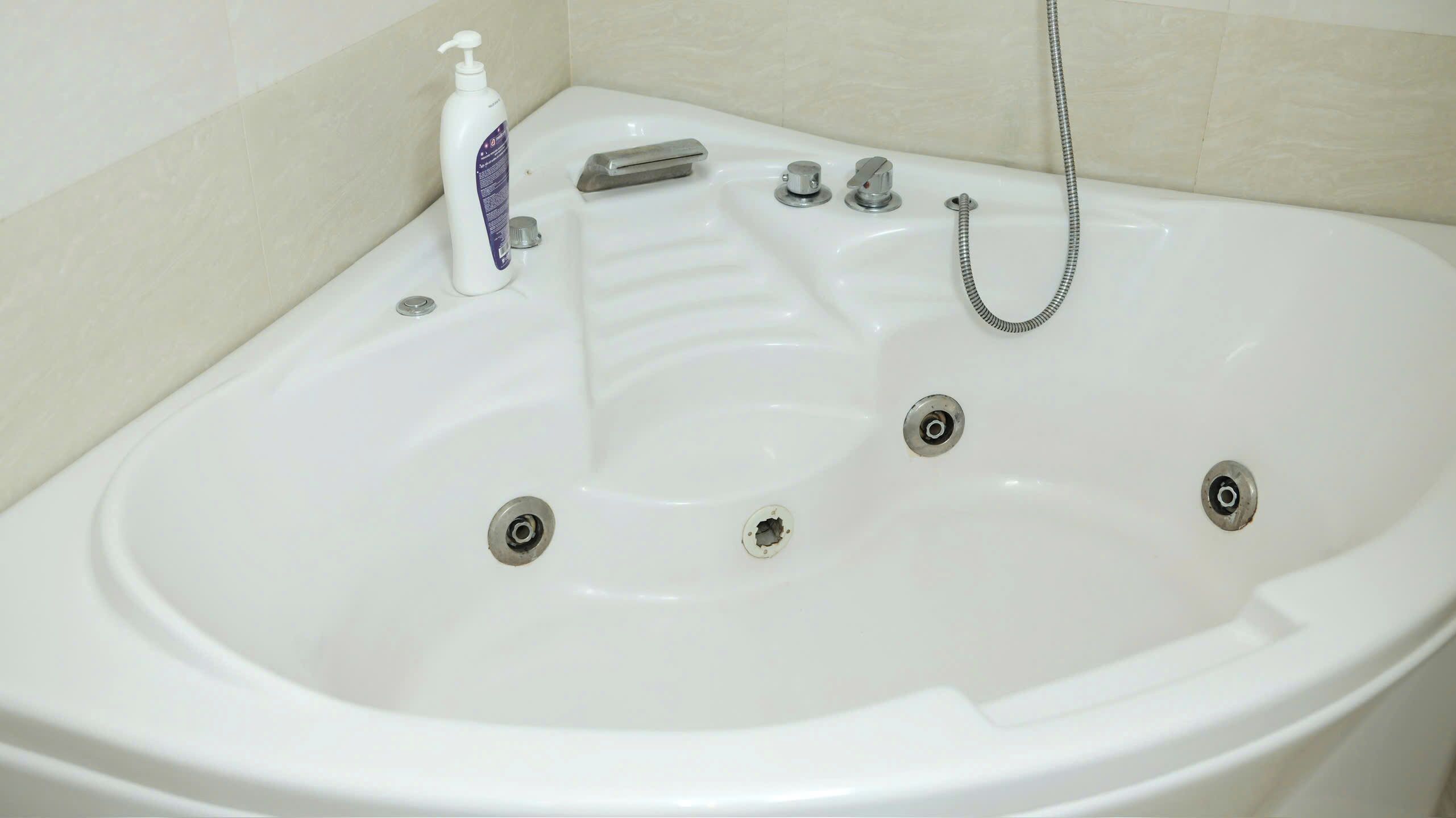 A white bathtub with a handheld showerhead, a bottle of shampoo, and a faucet.