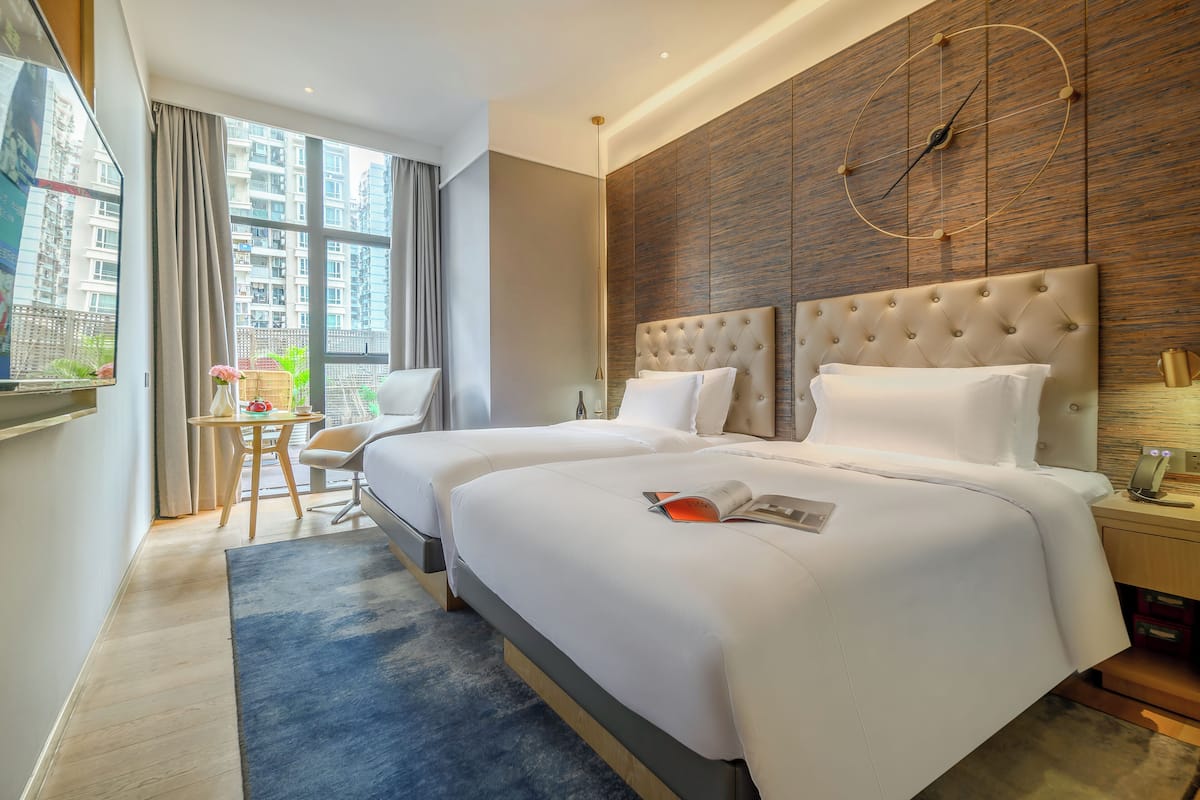 A hotel room with two beds, a large window, a wooden wall, and a clock.