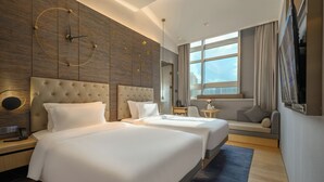 Ein modernes Hotelzimmer mit zwei großen Betten, einer Sitzecke, einem großen Fenster und einer Wanduhr.