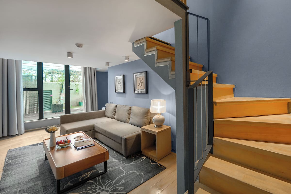 A modern living room with a sofa, coffee table, and lamp, a staircase, and a view of greenery outside.