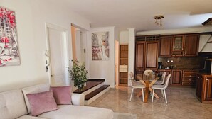 Un salon avec un canapé, une table à manger avec des chaises et un coin cuisine doté de meubles en bois et d’un plan de travail.