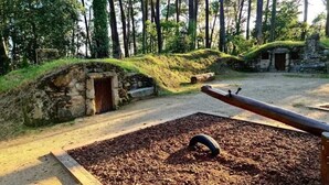 Un parc amb un camí de terra, una estructura de pedra amb una porta, i una zona de jocs infantils amb una balança i un pneumàtic.
