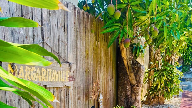 A wooden fence with a sign that reads 'MARGARITAVILLE,' a tree with green leaves, and a gravel pathway. - Mango Beach Retreat (Lake Worth)