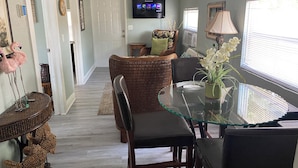 A dining area with a glass table, wicker chairs, and a television mounted on the wall. - Mango Beach Retreat (Lake Worth)