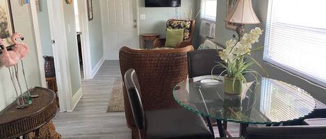 A dining area with a glass table, wicker chairs, and a television mounted on the wall.