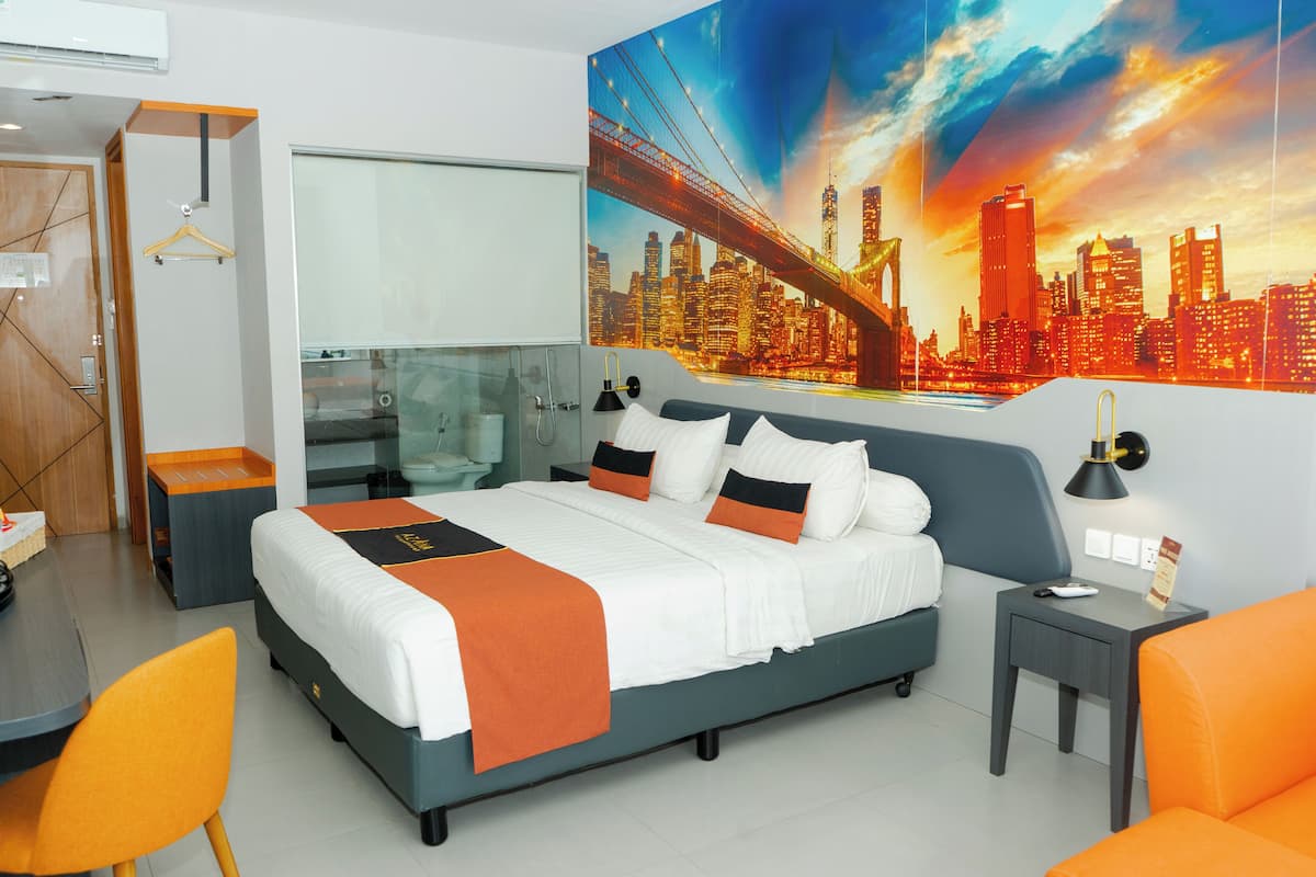 A modern hotel room with a large bed, a desk, and a chair. There is a cityscape painting on the wall and a window with a view of the city.
