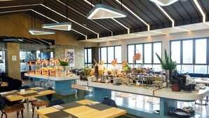 A modern restaurant with a central bar area, multiple seating options, and large windows providing natural light. - Azana Style Hotel Tulungagung (Tulungagung)