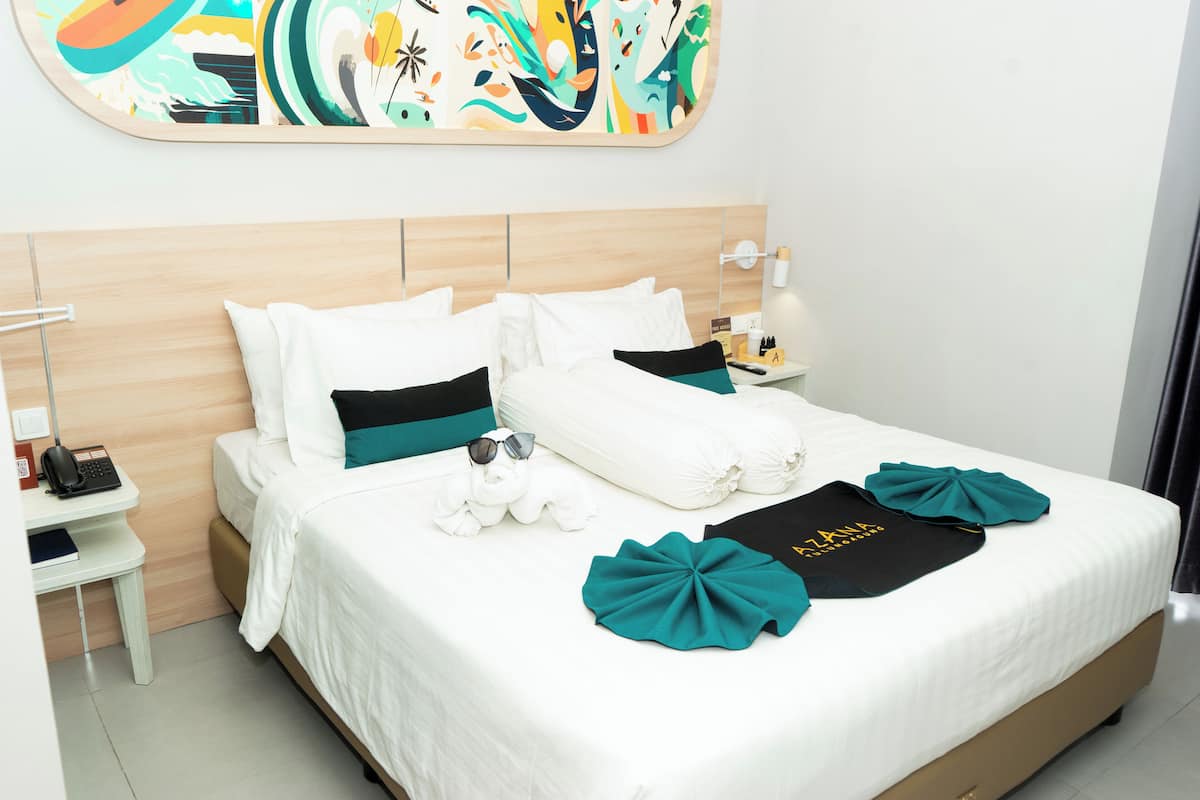 A neatly made bed with white and teal pillows, a black towel, and a teal decorative item on the bed.