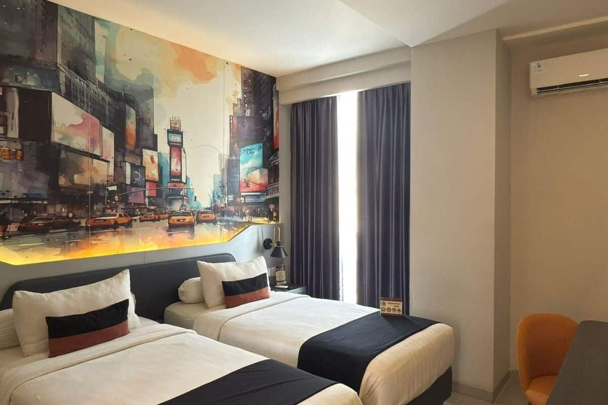 A hotel room with two beds, a cityscape mural, a desk, and a chair.