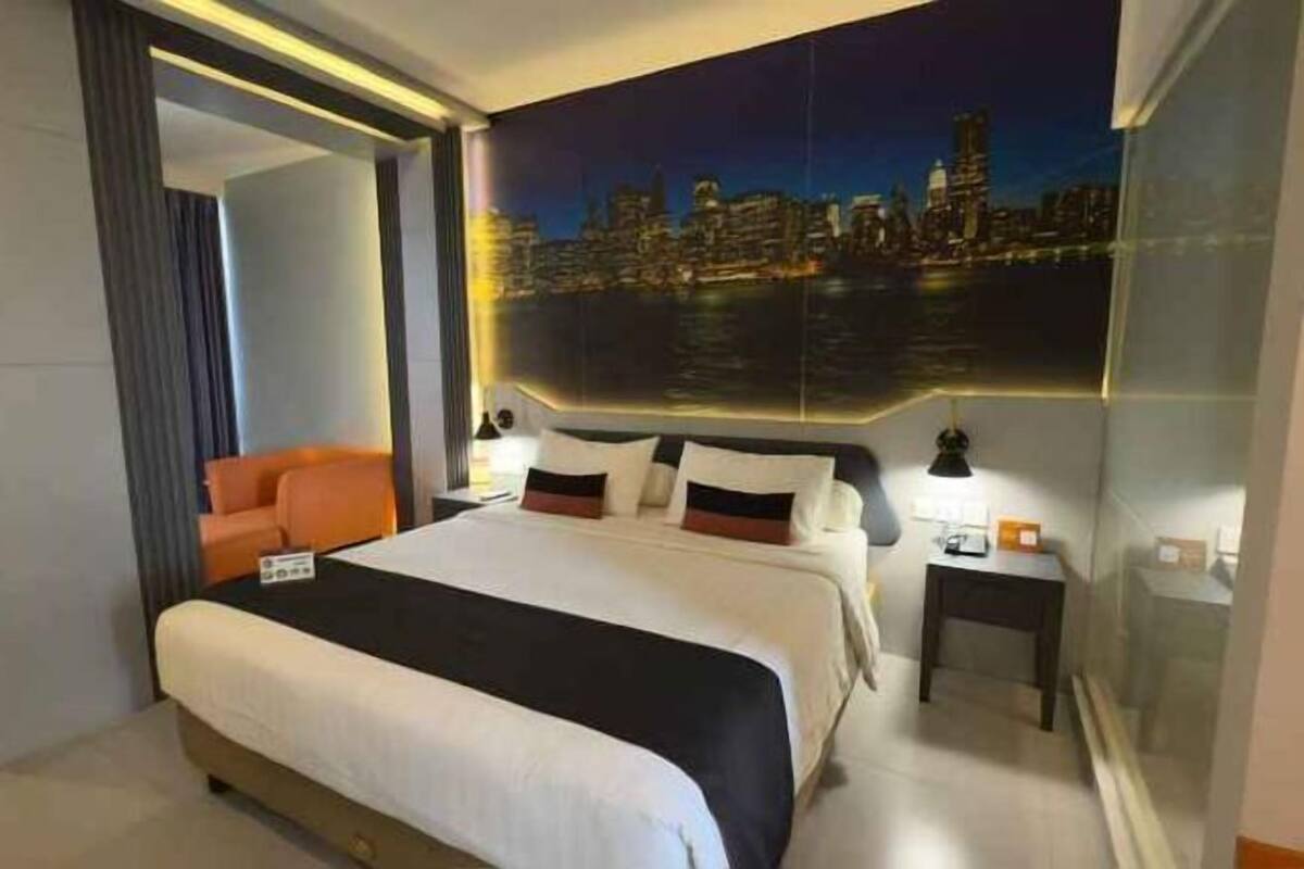 Una habitación de hotel moderna con una cama grande, un mural con vista a la ciudad, una mesita de noche y una silla naranja.