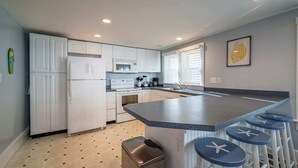 A modern kitchen with white cabinets, a microwave, stove, and a large island with bar stools. - OCHG Ocean Block 7-11 (Ocean City)